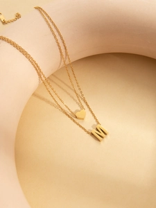 Detail of double-layer gold titanium steel necklace with heart and M letter pendants