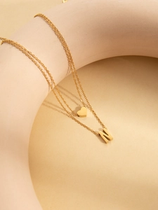 Detail of gold double-layer necklace featuring a heart charm and N-shaped letter pendant