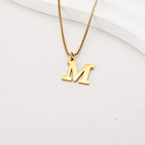 Detail of a gold letter M pendant on a box chain necklace with a metallic finish