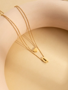 Close-up of gold double-layer necklace with heart and letter O pendant on minimalist props