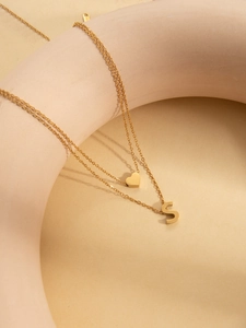Detail of double-layered gold necklace with heart charm and 3D S letter pendant