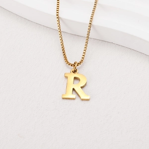 Macro detail of golden letter R pendant on a box chain over white textured background