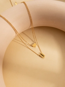 Close-up of double-layer gold necklace featuring a heart charm and a letter U pendant