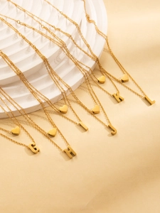 Detail of gold-plated double-layer letter necklaces on a white minimalist pedestal