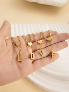 Close-up of a hand holding four gold-plated titanium steel necklaces spelling LOVE with hearts
