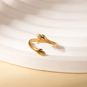 Detailed shot of adjustable gold hug ring with hands design on white display stand