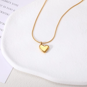 Minimalistische gouden hartjesketting voor dames op een wit getextureerd stenen dienblad