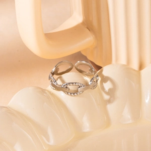 Macro shot of silver-tone hollow chain link ring on a cream ceramic tray