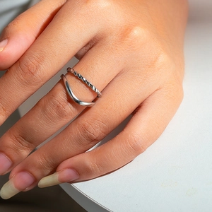 Detail of layered silver ring featuring twisted rope and minimalist wavy band designs