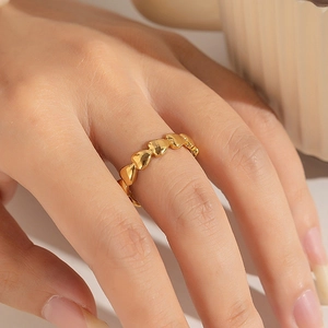 Détail d'une bague en acier doré avec des cœurs continus portée par un mannequin