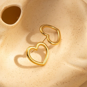 Detailed view of hollow heart-shaped gold-plated stainless steel earrings on a ceramic tray
