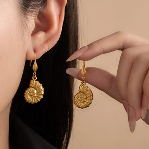 Detail of vintage matte gold snail shell pendant earrings worn by a model
