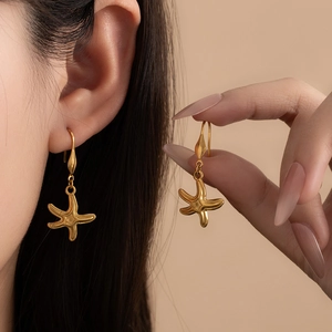 Detail of bohemian gold starfish drop earrings worn by a model in warm studio lighting