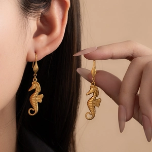 Macro detail of golden seahorse drop earrings with textured surface on model