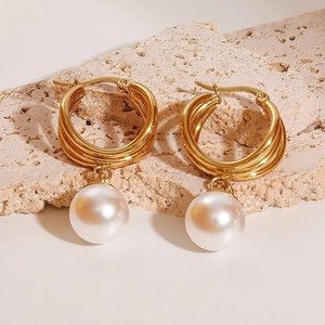 Eleganti orecchini multi-cerchio dorati con perle bianche su superficie in pietra