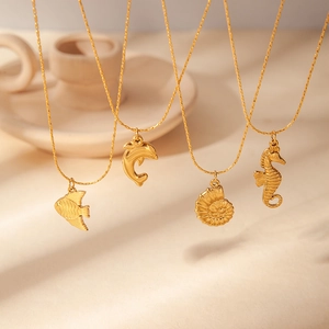Detail of four gold ocean-themed necklaces with fish, dolphin, shell, and seahorse pendants