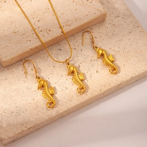 Detail of gold seahorse pendant necklace and earrings set on a textured stone surface
