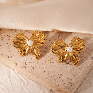 Detail of golden butterfly earring with white pearl on premium stone and silk backdrop