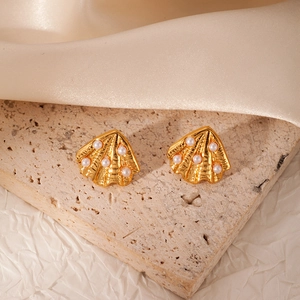 Detail of golden scallop shell earrings with white pearls on beige travertine stone