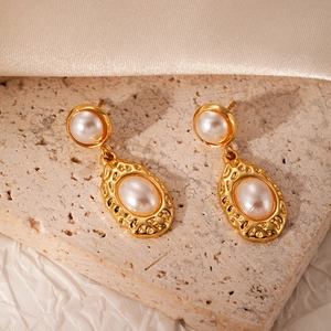 Close-up of pearl drop earrings with hammered gold texture on travertine stone surface