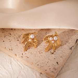 Golden radial feather earrings with white pearls on a minimalist travertine stone base