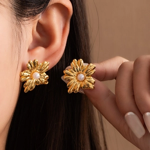 Close-up of artistic gold floral earrings featuring a lustrous white pearl center