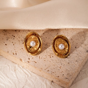 Dettaglio di orecchini dorati con trama a spirale e perla bianca in stile vintage
