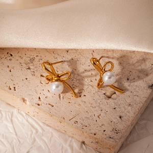 Detail shot of golden bow earrings with white pearl center on textured backgrounds