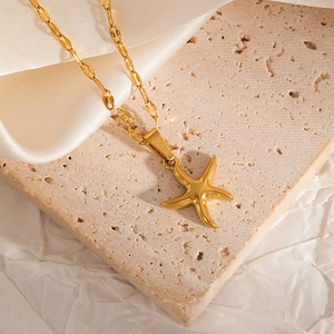 Macro shot of gold-plated starfish pendant necklace on textured stone and satin fabric