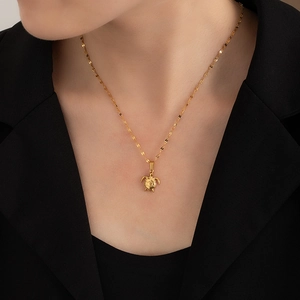 Detail of a golden sea turtle pendant necklace on a model wearing a black blazer