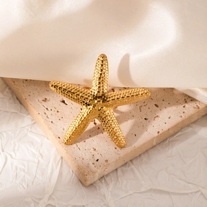 Detail of a golden starfish open ring featuring textured beads on a beige stone surface