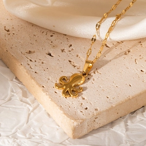 Detailed view of a gold-plated octopus pendant on a flat lip chain over silk fabric