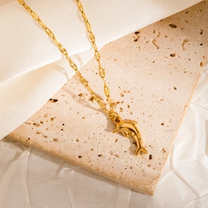 Detailed close-up of a golden dolphin pendant on a twisted chain over white silk