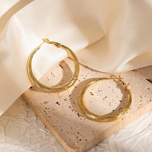 Polished 18k gold plated hoop earrings with twisted texture on light stone surface