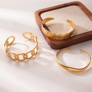Detailed close-up of a three-piece gold plated stainless steel cuff bracelet set on a wooden tray