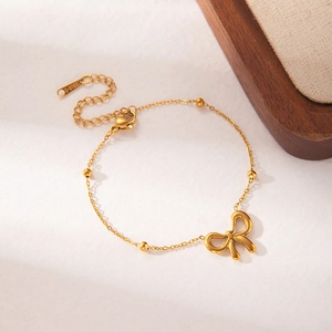 Detail of gold stainless steel bow bracelet with tiny beads and a heart charm tag
