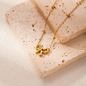 Detail view of a gold bow pendant necklace with bead accents on a textured stone tray