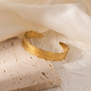 Detail of gold-plated open bangle with fine feather texture on a travertine stone base
