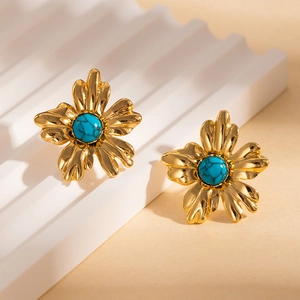 Détail de boucles d'oreilles fleur dorée avec pierre turquoise sur socle blanc