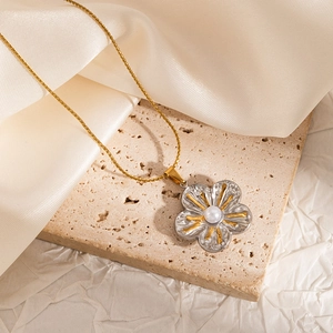 Detailed shot of a floral pendant necklace with a pearl center on a beige textured stone
