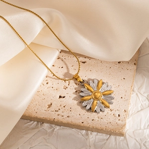Detailed macro view of a gold daisy pendant necklace on a beige stone and silk background