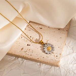 Detailed macro of a two-tone daisy pendant necklace on cream satin and stone base