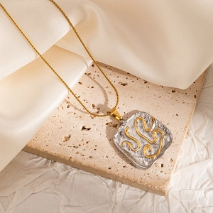 Macro view of abstract square pendant with gold curves on textured steel