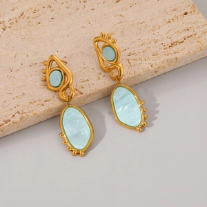 Detail view of gold earrings with blue resin accents on a textured stone display