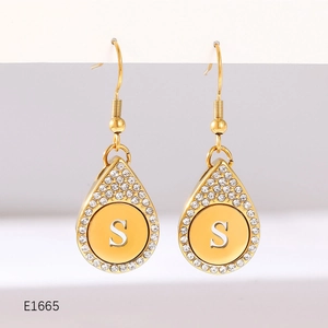 Detail of gold teardrop earrings with pavé diamond halo and initial S letter charm