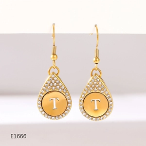 Detail of gold-plated drop earrings featuring a crystal-encrusted letter T pendant