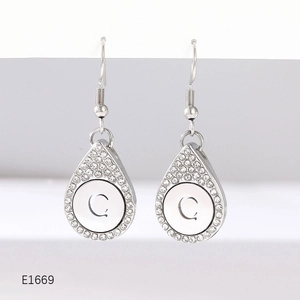 Close-up of silver teardrop earrings with pavé crystals and letter C engraving