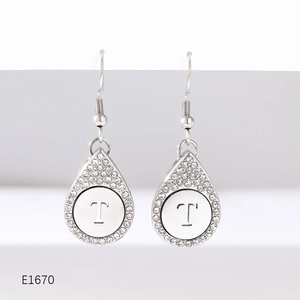 Detail of silver drop earrings with crystal pavé edges and an engraved letter T