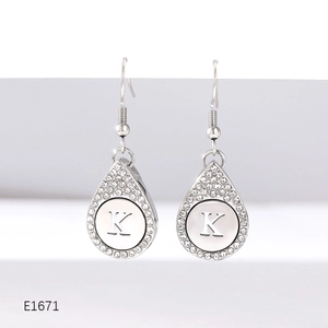 Macro shot of silver-tone teardrop earrings featuring a crystal-set K letter disc pendant