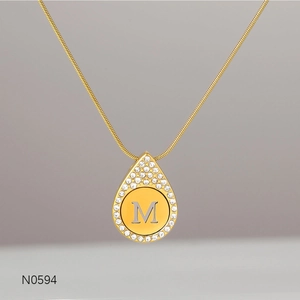Close-up of golden teardrop necklace pendant with crystal border and M letter detail